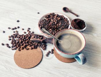 Fresh tasty coffee. Coffee cup, roasted coffee beans, ground powder and beer coaster on light wooden background.