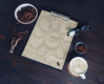 Kraft stationery and coffee. Clipboard with blank kraft paper letterhead, coffee cup, coffee beans, glasses and coffee ground on vintage wood table background.