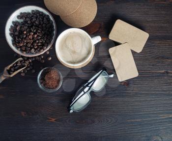 Still life with coffee cup, kraft business cards, coffee beans, glasses and ground powder on old wooden background. Top view. Flat lay.