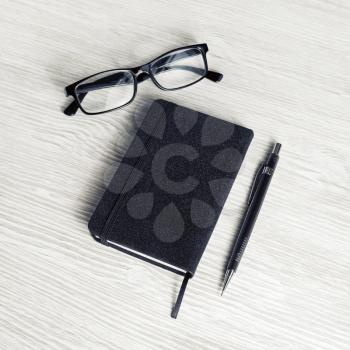 Photo of closed blank black notebook, glasses and pencil on light wood table background.