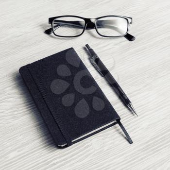 Blank black notepad, glasses and pencil on light wooden background.