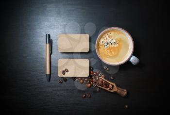 Photo of blank kraft business cards, coffee cup, coffee beans and pen on black wooden background. Responsive design mockup. Top view. Flat lay.