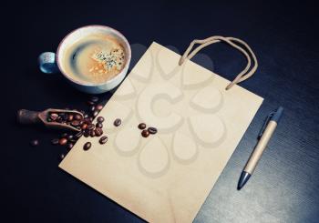 Blank kraft paper bag, coffee cup, coffee beans and pen on black table background. Responsive design template.