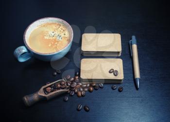Photo of blank kraft business cards, coffee cup, coffee beans and pen on black wooden background. Responsive design mockup.
