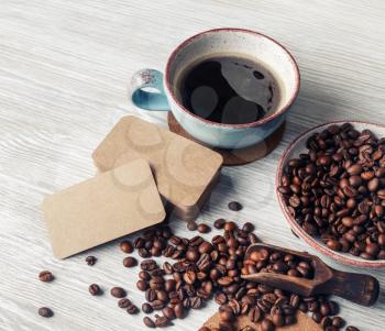 Delicious fresh coffee. Blank kraft paper business cards, coffee cup and coffee beans on kitchen table background.