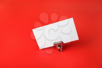 Blank business card and metal binder clip on red paper background. Copy space for text.
