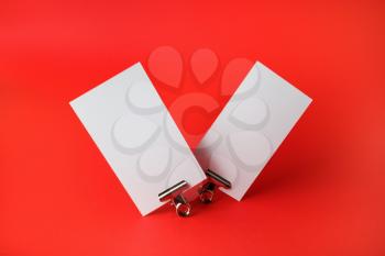 Two blank business cards and metal binder clips on red paper background. Branding ID template.