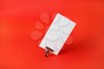 Photo of blank business card and metal binder clip on red paper background. Corporate identity template.