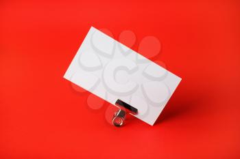 Blank white business card and metal binder clip on red paper background. Branding ID template.