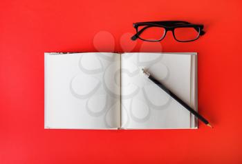 Mockup of opened blank brochure, pencil and glasses on red background. Template for placing your design. Flat lay.