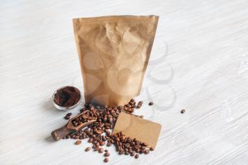 Blank kraft paper coffee package, coffee beans, ground powder and vintage business cards on light wooden background.