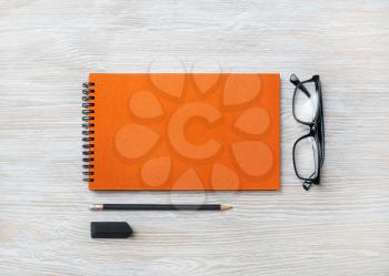 Orange notebook, glasses, pencil and eraser on light wood table background. Top view. Flat lay.