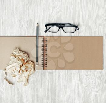 Blank open sketchbook, glasses, pencil and crumpled paper on light wooden background. Responsive design mockup. Top view. Flat lay.