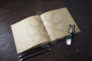 Opened book with blank craft paper pages, pencils and glasses on wooden background.