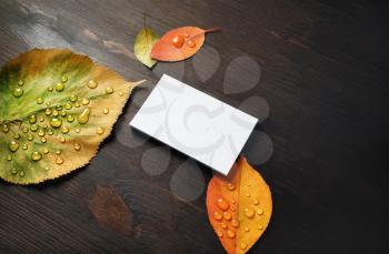 Photo of blank business card and bright autumn leaves on wooden background. Template for branding identity. Mockup for ID.