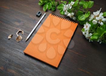 Blank orange notepad, pencil, sharpener and flowers on wood table background.
