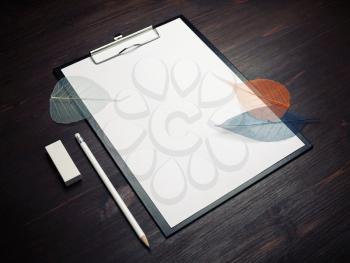 Clipboard with blank white sheet of paper, pencil, leaves and eraser on wooden background. Responsive design template.