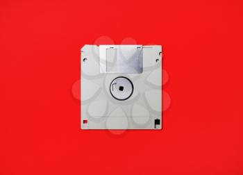 Gray diskette on red paper background. Floppy disc. Flat lay.