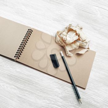Photo of kraft notepad, pencil, eraser and crumpled paper on light wood table background.