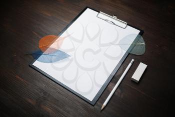 Blank stationery template. Clipboard with blank letterhead, pencil, eraser and leaves on wood table background.