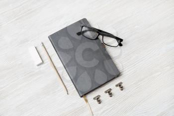 Photo of blank closed notebook, glasses, pencil and eraser on light wood table background. Responsive design mockup. Stationery elements.