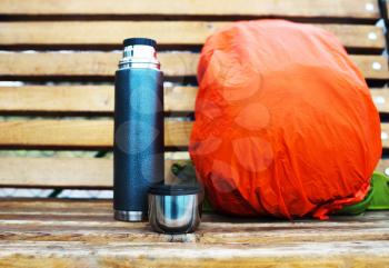 Horizontal thermos with backpack on bench bokeh background

