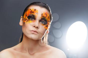 Portrait of a girl with an original make-up. Beauty close-up with orange and red rhinestones on a face of the model