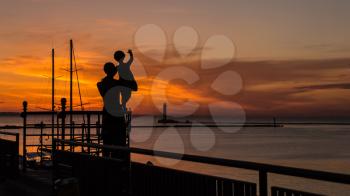 Silhouettes of mother and child against the background of the rising sun in the seaport