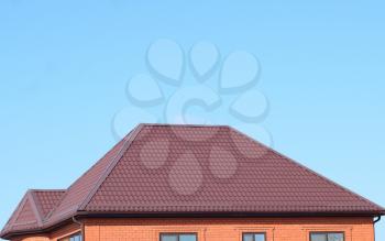 A house with a roof made of metal sheets. The house with gables, windows and metal roof, equipped with overflow and protection from snow.