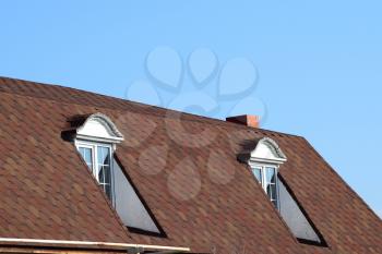 A house with a roof made of metal sheets. The house with gables, windows and metal roof, equipped with overflow and protection from snow.