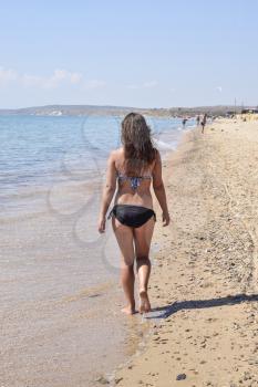 Girl walking on the beach, rear view. Walk the dark-haired woman in a swimsuit along the coastline on the sea beach.