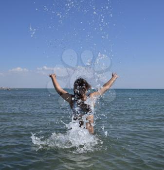 She sprinkles in seawater. Flying up spray from the water throws. The girl with dark hair and a bathing enjoys sea.