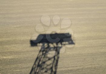 The shadow of a water tower on a plowed field.