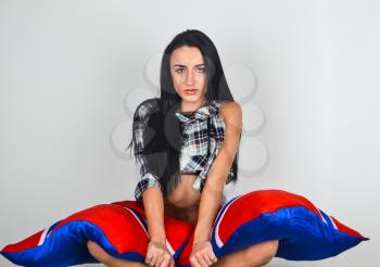 Girl brunette in a plaid shirt sitting in the lotus position and covers the legs red blue cushions.