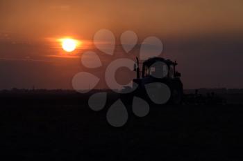 Tractor plowing plow the field on a background sunset. tractor silhouette on sunset background.