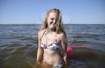 Blond girl in a bikini standing in the sea water. Beautiful young woman in a colorful bikini on sea background