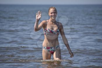 Blond girl in a bikini coming out of the sea water. Beautiful young woman in a colorful bikini on sea background.