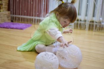 One year old baby girl sitting on the floor. A child playing with wicker balls. A blonde girl.