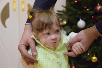 Year-old girl with dad in the background of the Christmas tree. A child with gray eyes and blond hair.