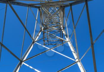 Supports high-voltage power lines against the blue sky. View from the bottom up.