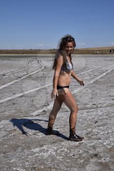 Girl standing on the dry bottom of a salt lake. Walk the dark-haired woman in a swimsuit on the bottom of a dry lake with salt and mud. The ancient dried-up lake.