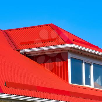 House with plastic windows and a red roof of corrugated sheet. Roofing of metal profile wavy shape on the house with plastic windows.
