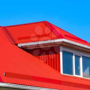 House with plastic windows and a red roof of corrugated sheet. Roofing of metal profile wavy shape on the house with plastic windows.