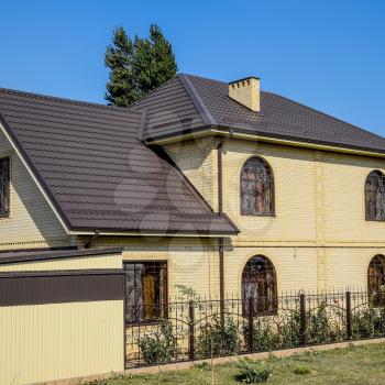 House of yellow brick and brown corrugated roof made of metal. Lattices on the windows