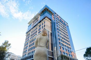 A girl with a beautiful figure in a gray dress near a tall building