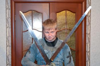 A man dressed up in a knight's hauberk at home in his room. Knight's sword in the hands of a man. Knightly chain armor and sword. Fitting of a knightly armor.