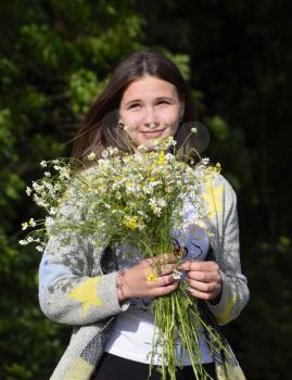 Young beautiful woman is standing in the forest with a bouquet of chamomiles.