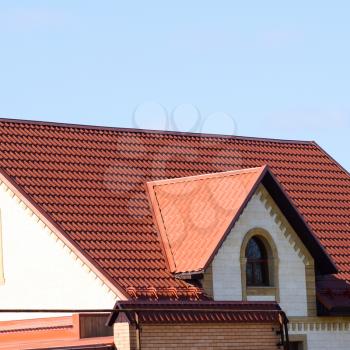 A house with a roof made of metal sheets. The house with gables, windows and metal roof, equipped with overflow and protection from snow.