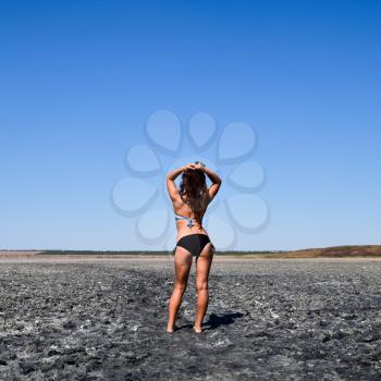 Girl standing on the dry bottom of a salt lake. Walk the dark-haired woman in a swimsuit on the bottom of a dry lake with salt and mud. The ancient dried-up lake.