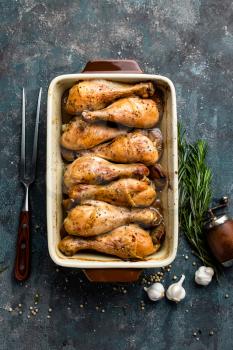 Grilled fried roast chicken legs, drumsticks on dark background, meat with ingredients for cooking, top view